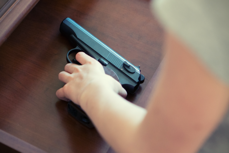 Child's hand reaching for a hand gun.
