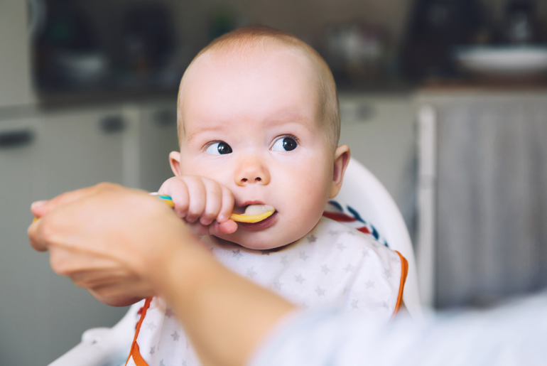 Baby is helped by parent to put a spoonful of baby food in his or her mouth.
