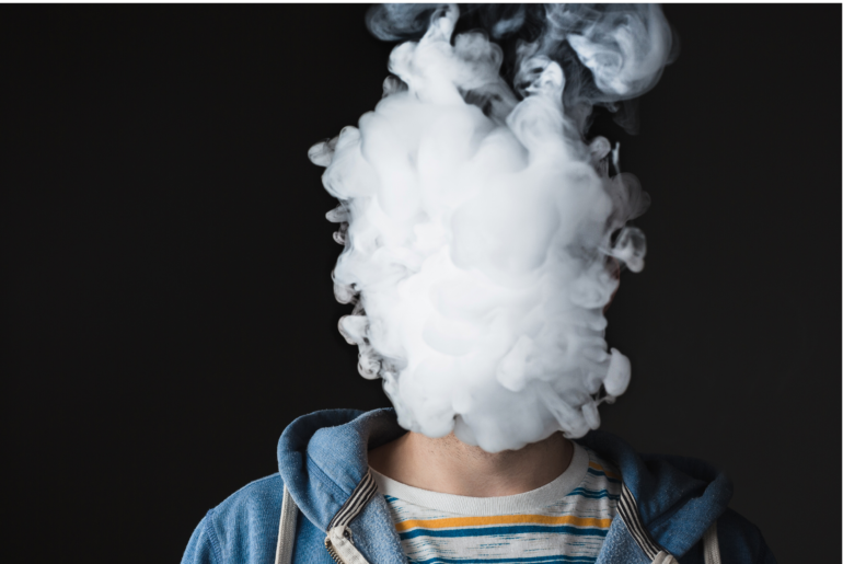 Young man blowing a cloud of vape fumes.