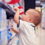 A toddler in a super market aisle points at a package.