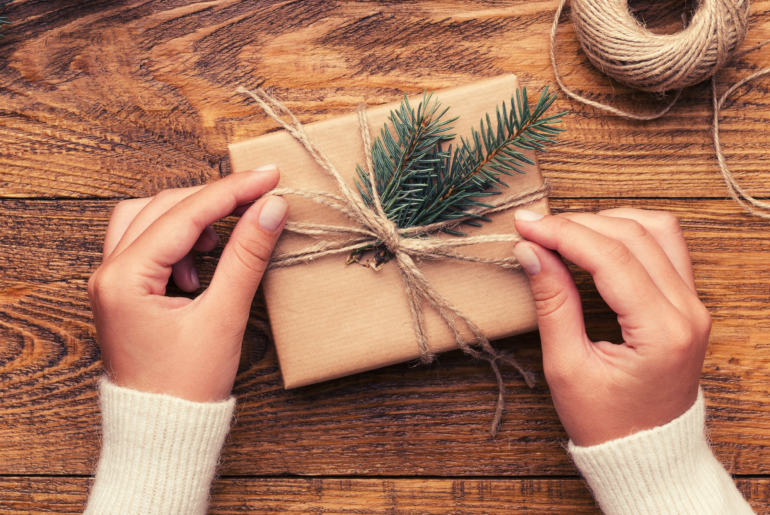 Close up of hands putting a twine bow on a wrapped present.