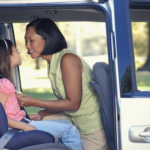 Mother strapping daughter into car seat.