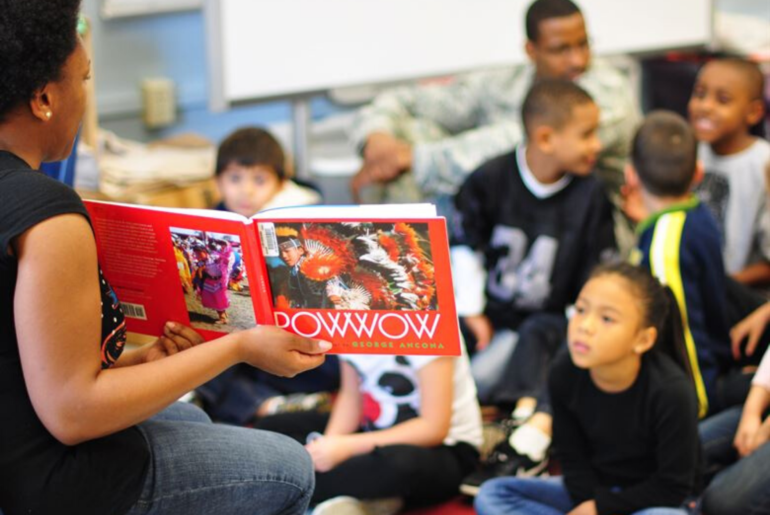 Elementary school students looking at a book about Pow Wow ceremonies.